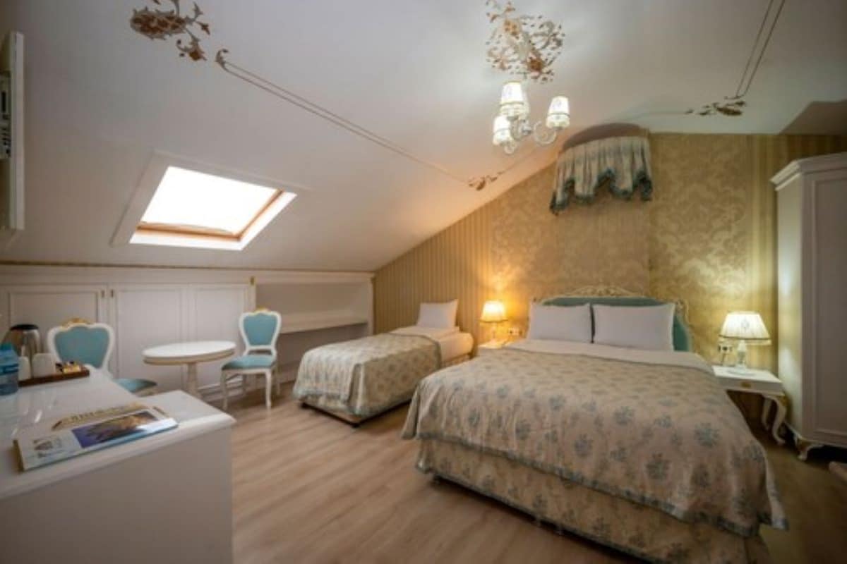A bedroom with two beds, a skylight, a desk with chairs, and a bedside table with lamps.