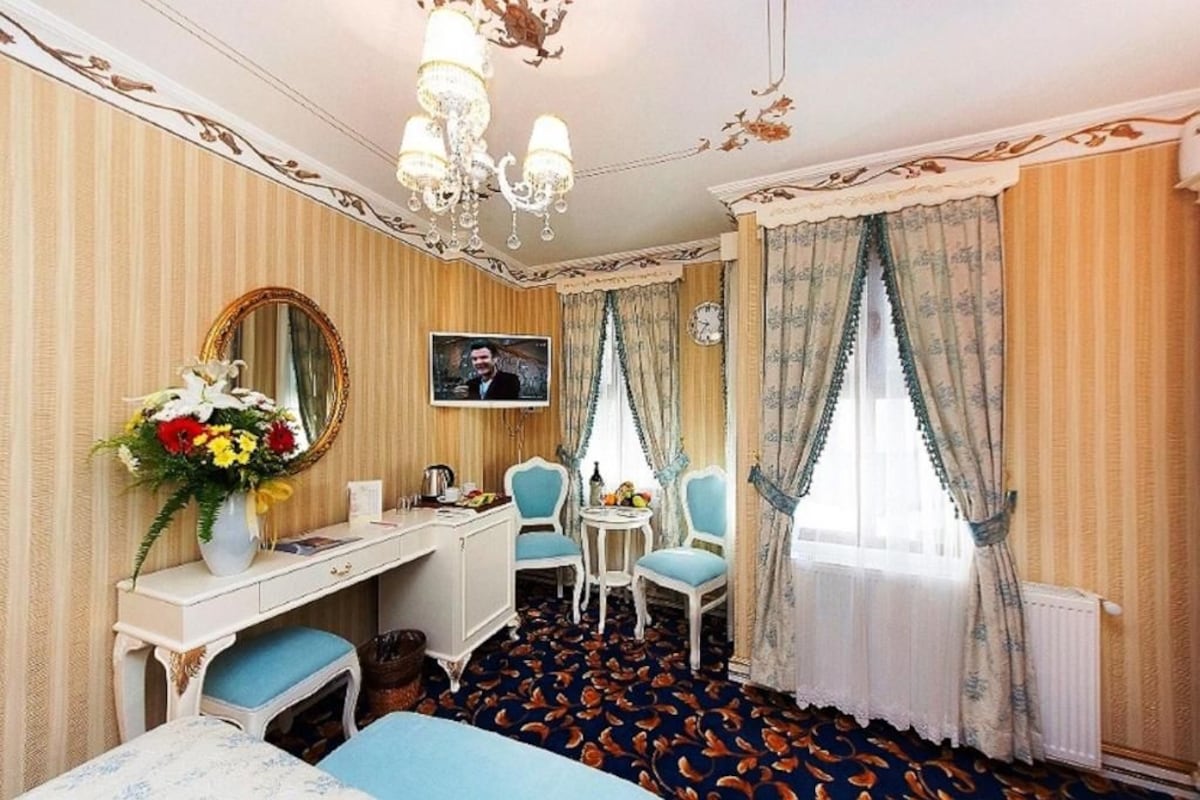 A hotel room with a bed, a desk, a chair, a mirror, a television, and a window with curtains.
