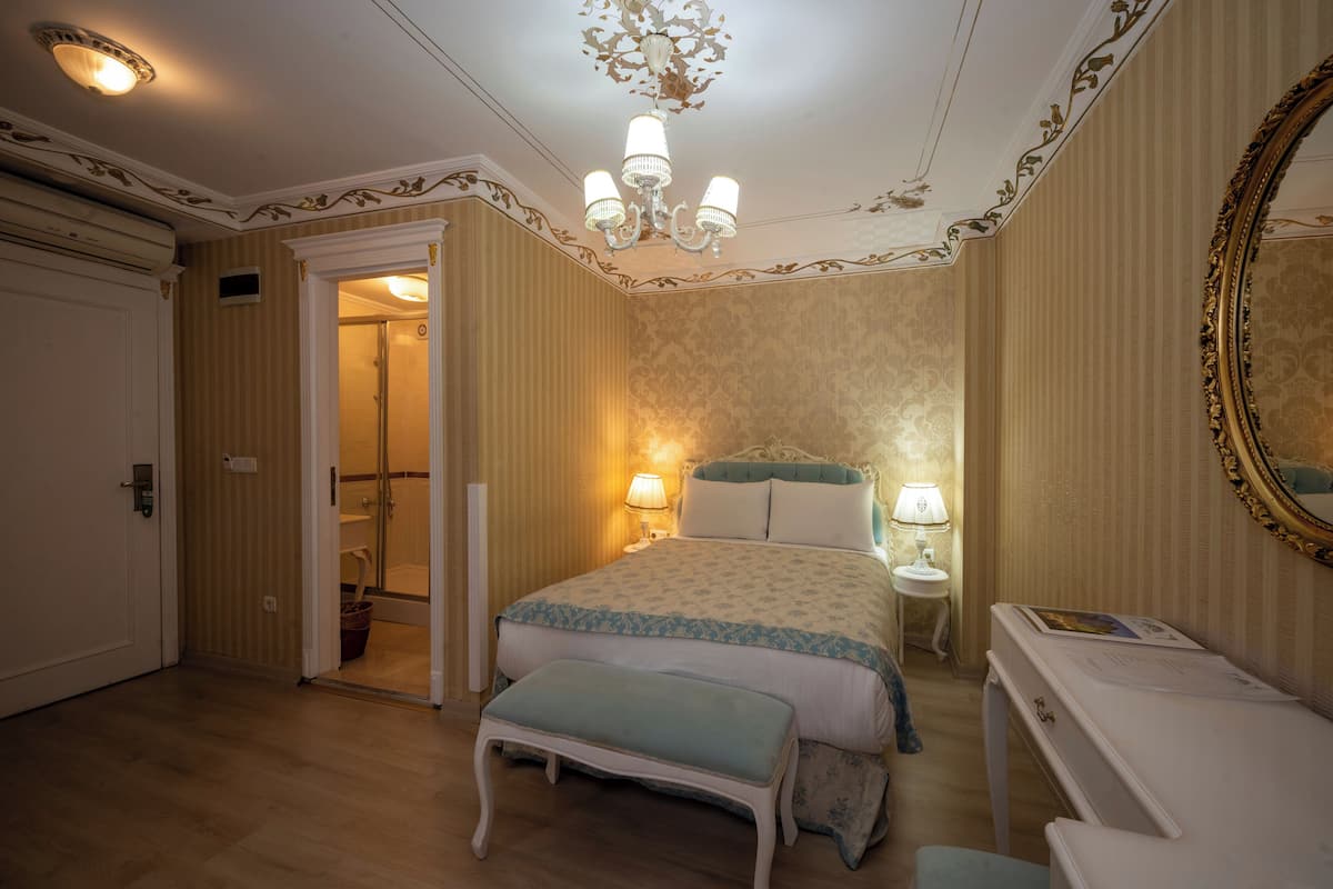 Une chambre à coucher comprenant un lit, des tables de chevet, une commode, un banc, un miroir et un lustre.