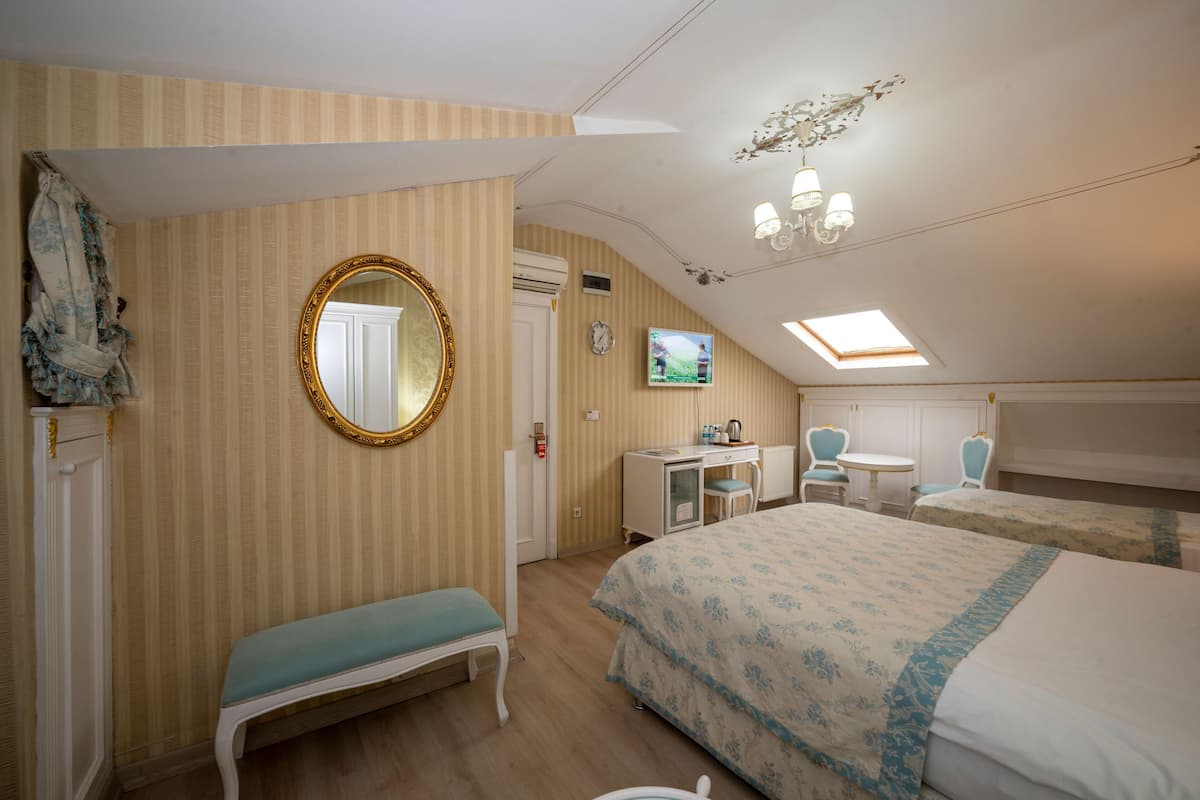 Une chambre d’hôtel équipée d’un lit, d’une banquette, d’un bureau, d’une télévision et d’un luminaire au plafond.