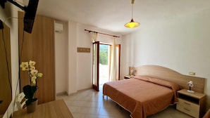 A bedroom with a bed, bedside tables, a desk, a chair, a potted plant, and a window with curtains.