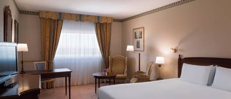 A hotel room with a bed, a desk, a chair, a television, and a window with curtains.