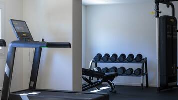 A home gym with a treadmill, dumbbells, and a weight machine.