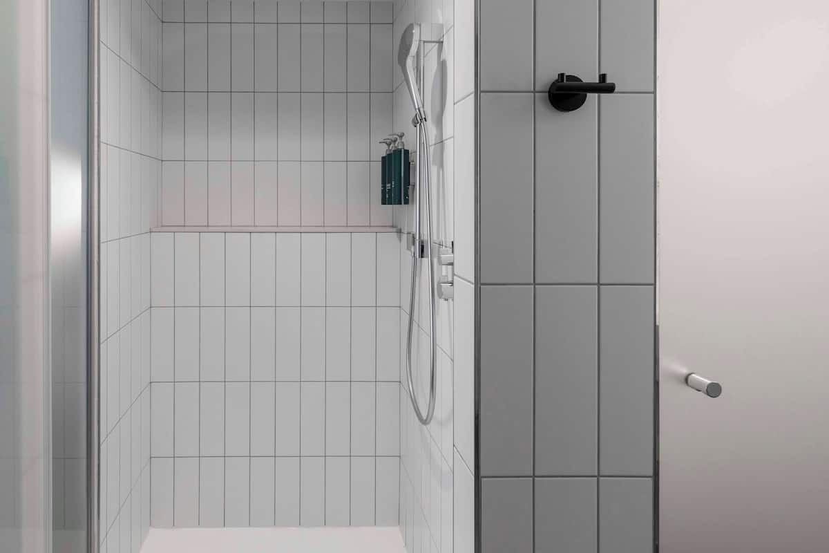 A modern bathroom with white tiles, a shower area, and a toilet.