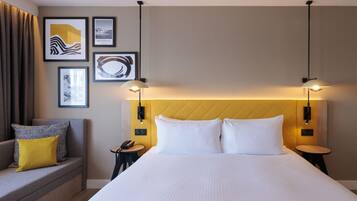 Habitación de hotel con una cama grande, un sofá con cojines, una mesita y obras de arte colgadas en la pared.