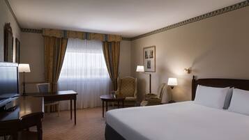A hotel room with a large bed, a desk, a chair, a television, and a window with curtains.