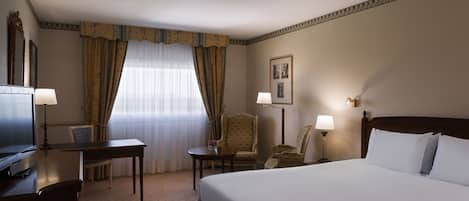 Habitación de hotel con una cama grande, un escritorio, una silla, un televisor y una ventana con cortinas.