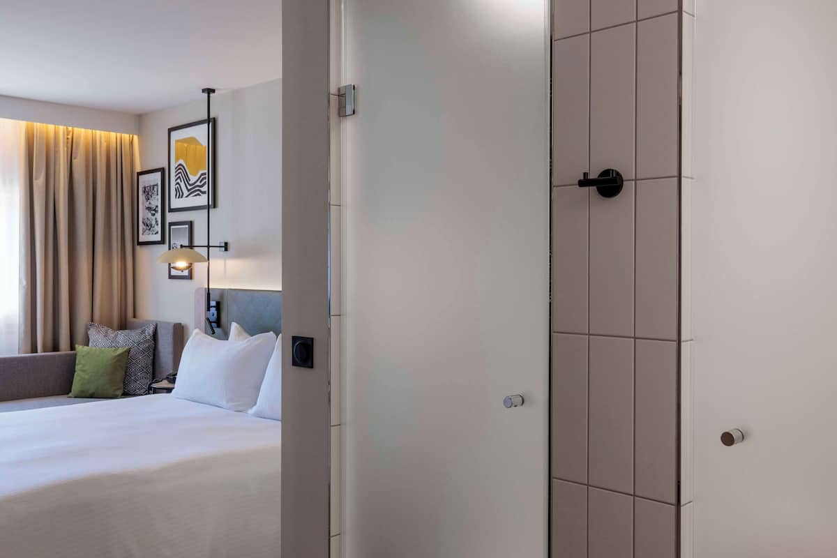 A hotel room with a bed, a headboard, a nightstand, a lamp, and a wall with framed artwork.