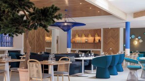 Interior de restaurante moderno com paredes de madeira, mobiliário azul e branco e uma árvore central.
