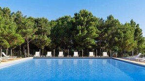 Piscina com espreguiçadeiras brancas e árvores ao fundo.