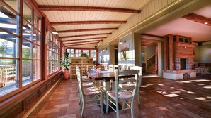 Une salle à manger spacieuse avec une longue table et des chaises, de grandes fenêtres et une cheminée en briques.