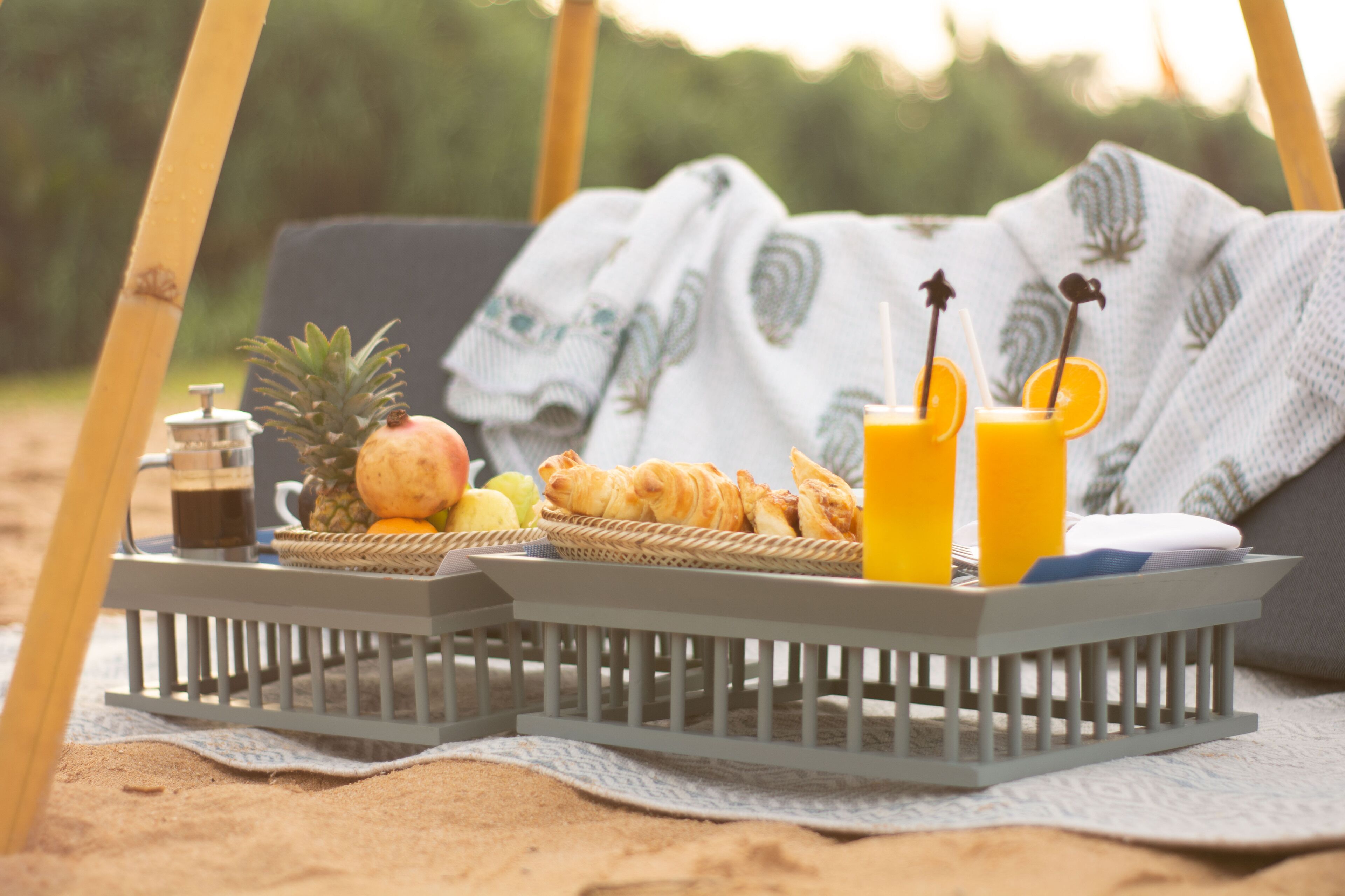 Un montaje para picnic en la playa con una cesta que contiene comida y bebidas, una piña y una botella de jugo.