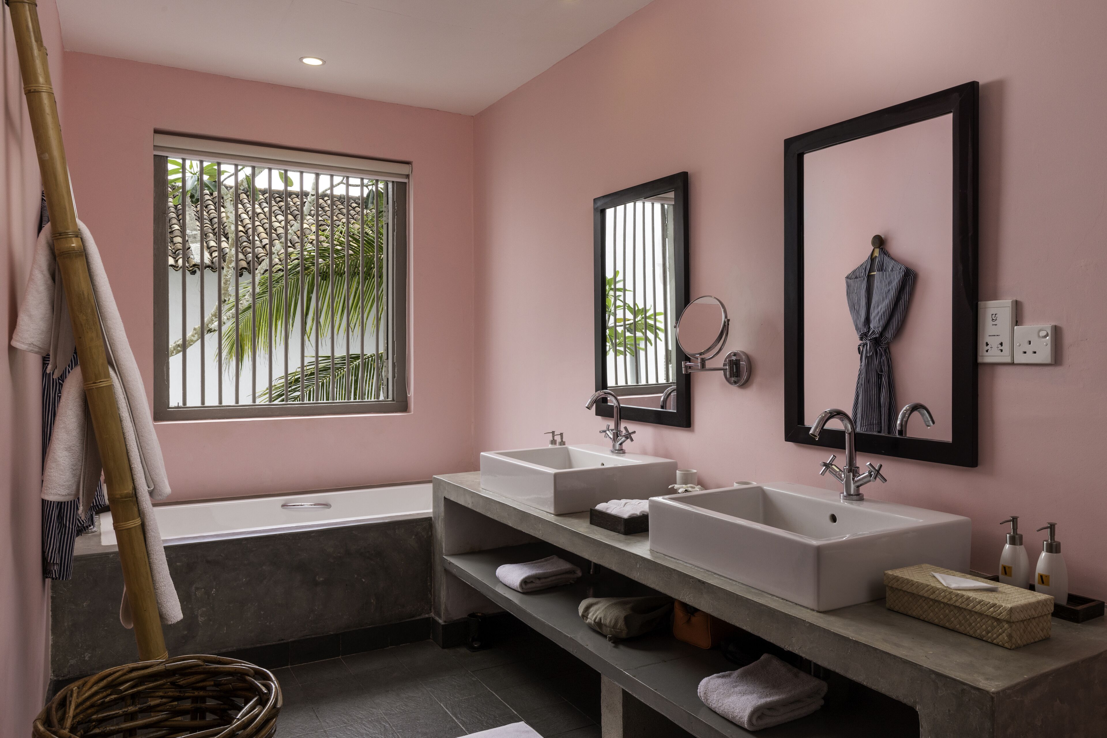 Ein modernes Badezimmer mit zwei Waschbecken, einer Badewanne und einem großen Fenster mit Blick auf Palmen.