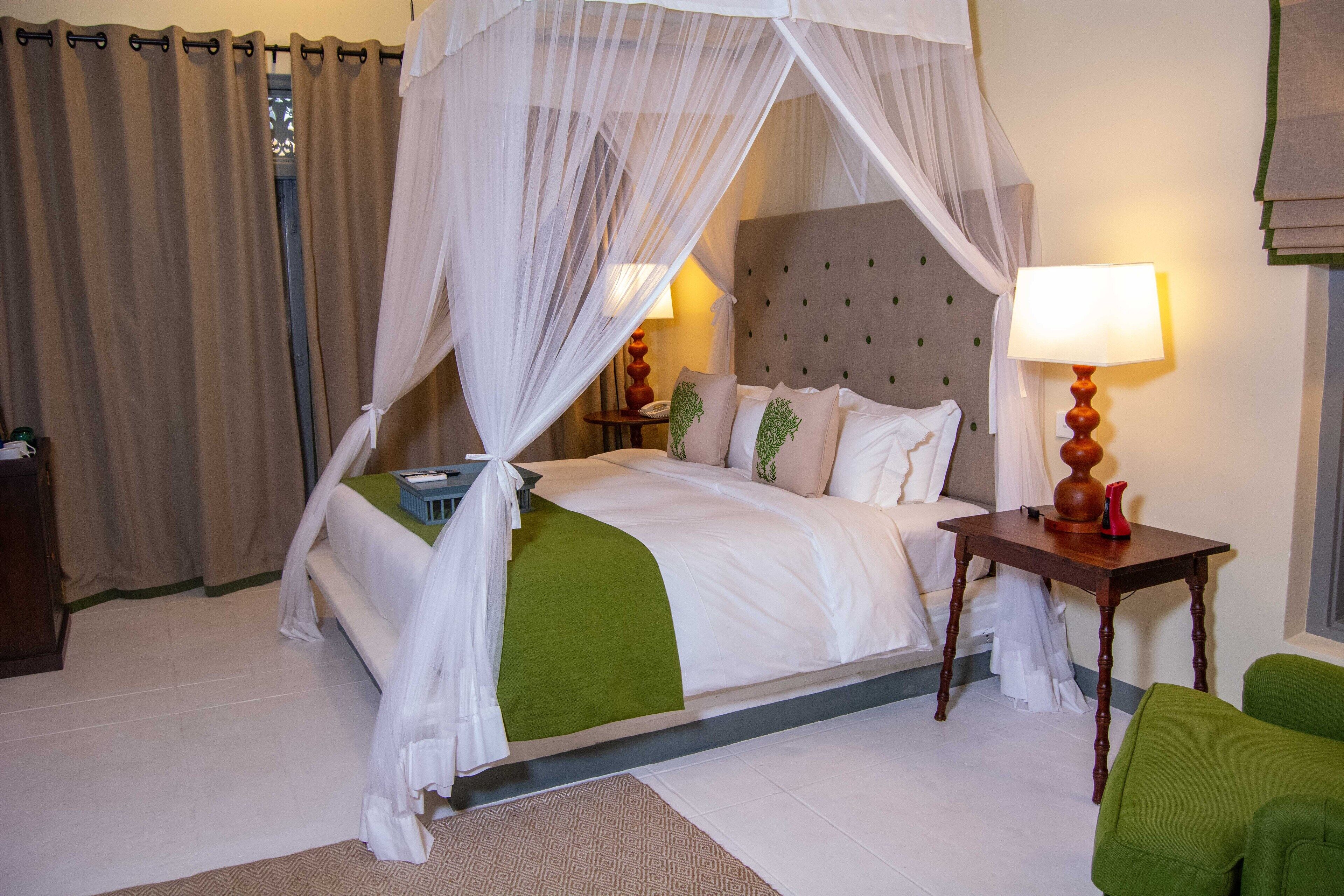 A neatly arranged hotel room with a bed, a bedside table with a lamp, and a green chair.