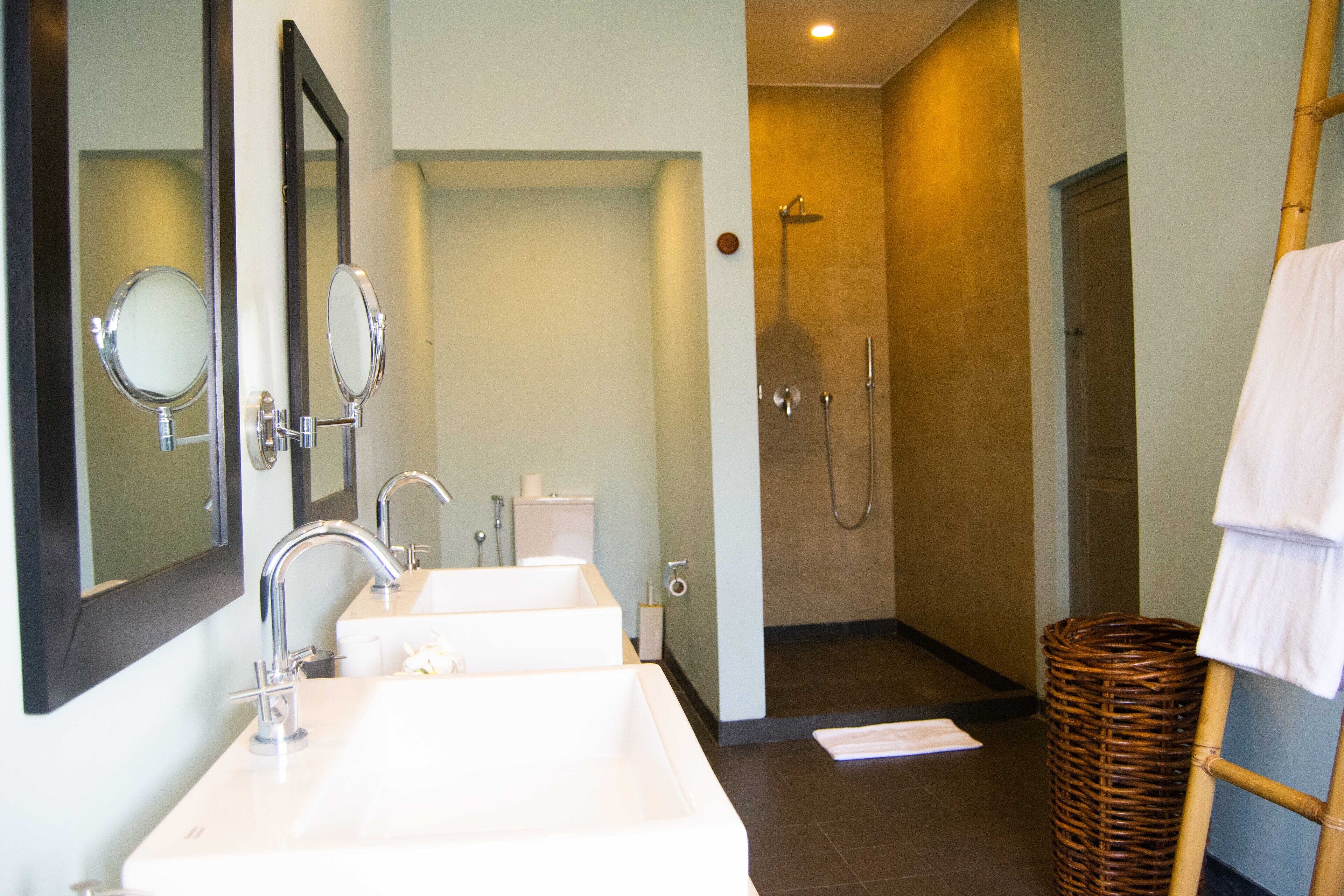 A bathroom with two sinks, a mirror, a shower, and a wicker basket.