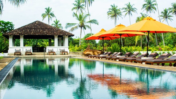 A swimming pool with lounge chairs and umbrellas, surrounded by palm trees. - The Villa Bentota by KK Collection (Bentota)