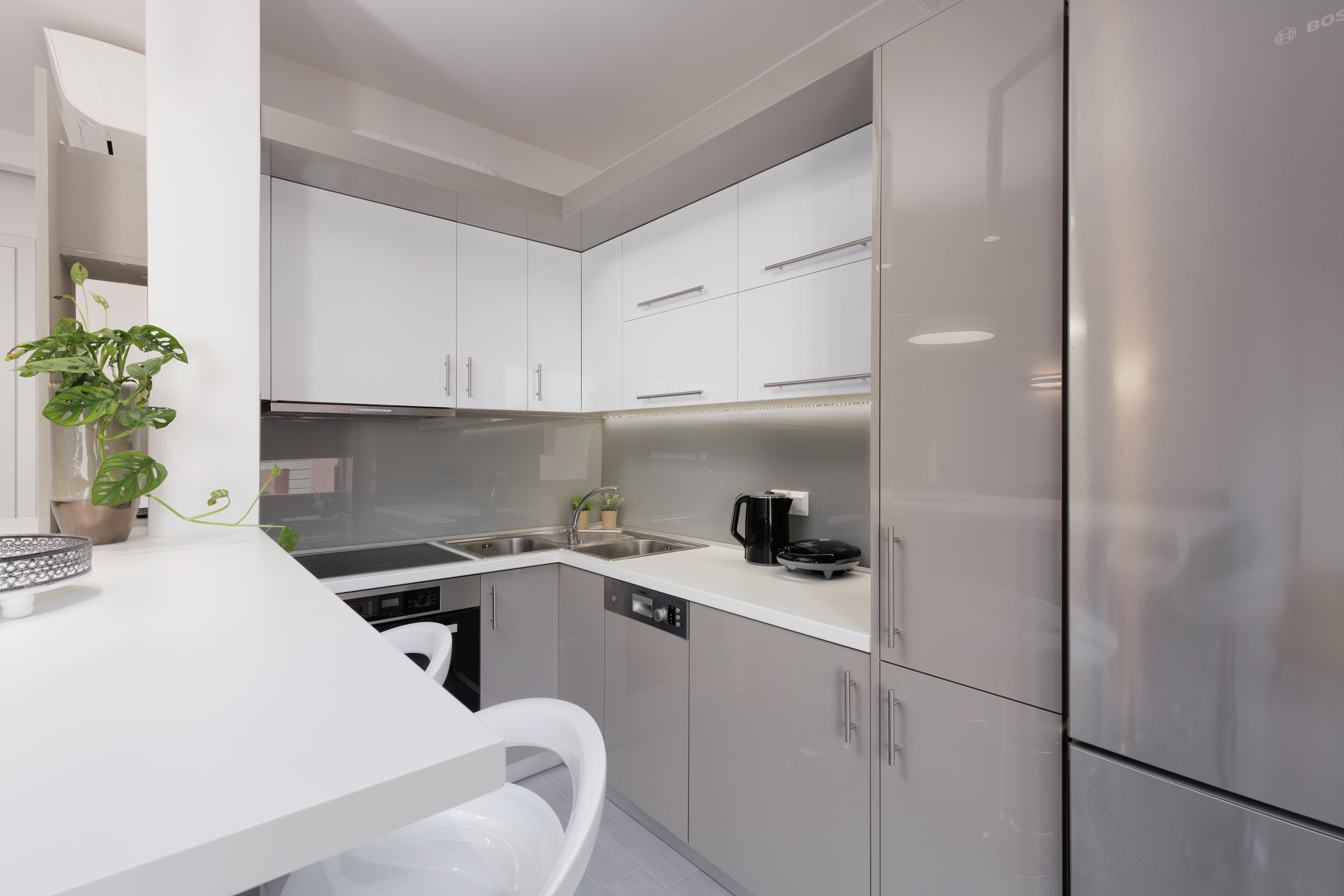 Une cuisine moderne avec des armoires blanches, des appareils en acier inoxydable et un plan de travail blanc.