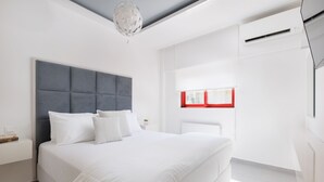 A modern bedroom with a large bed, a grey headboard, white bedding, a bedside table with a lamp, and a window with red blinds. -  A Luxury Retreat in Corfu Town by Konnect, Two-Bedroom Apartment (Corfu)