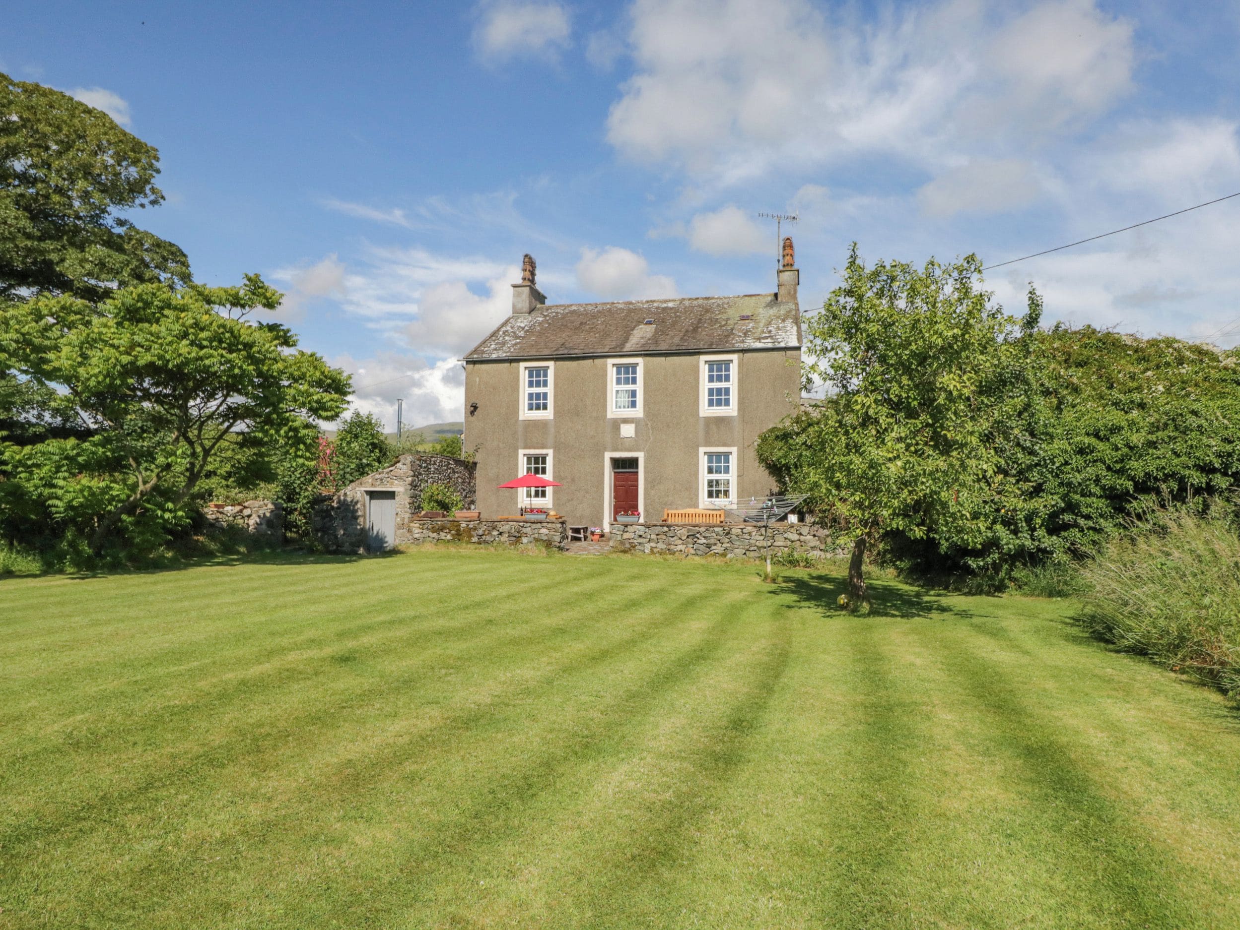 A two-story house with a red door, a stone wall, and a well-maintained lawn.