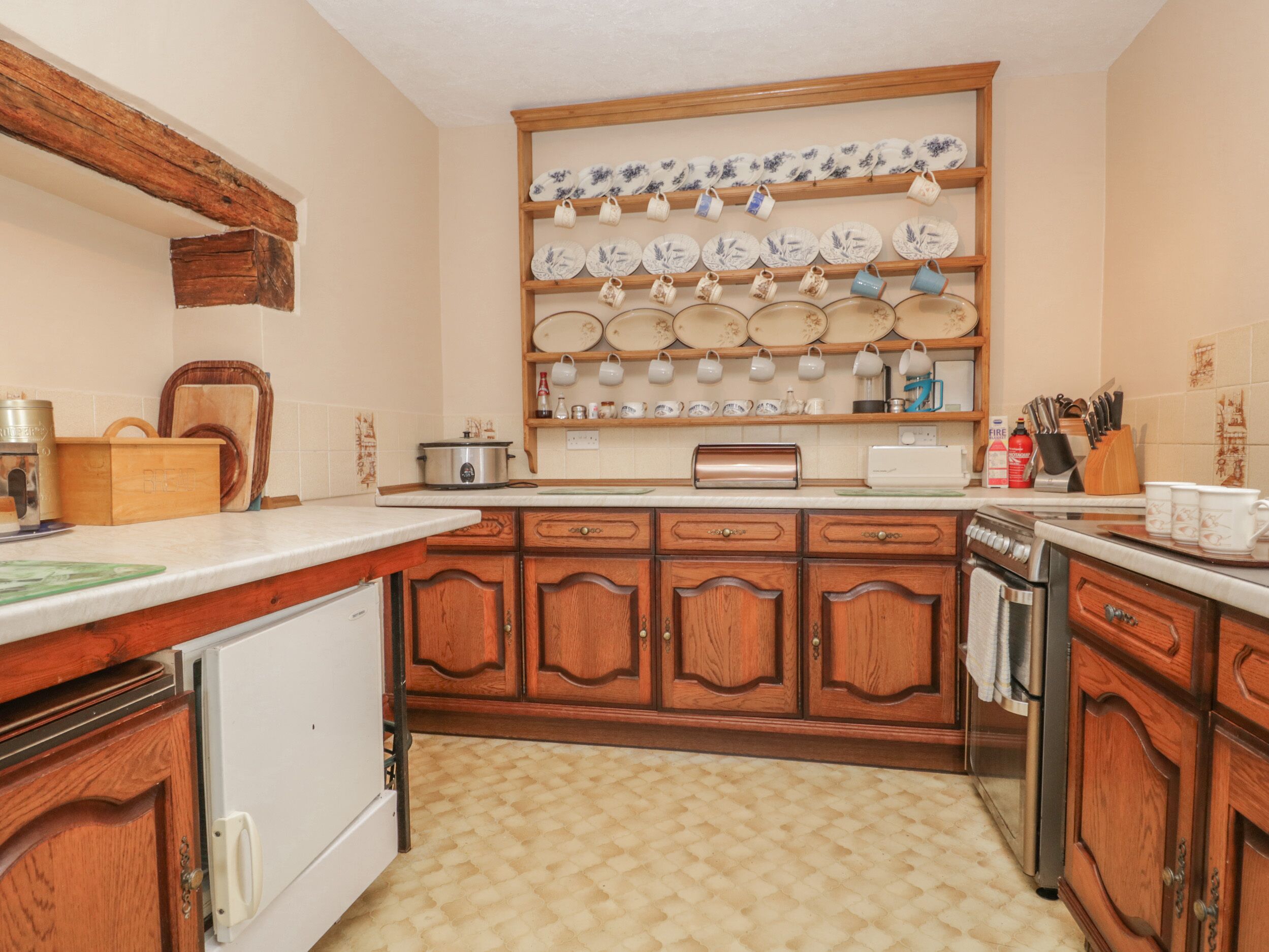 Una cocina con armarios de madera, encimera, estufa, lavabo y una repisa con vajilla.