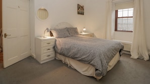 Une chambre à coucher avec un lit, des tables de chevet, un miroir, une fenêtre avec des rideaux et une porte.
