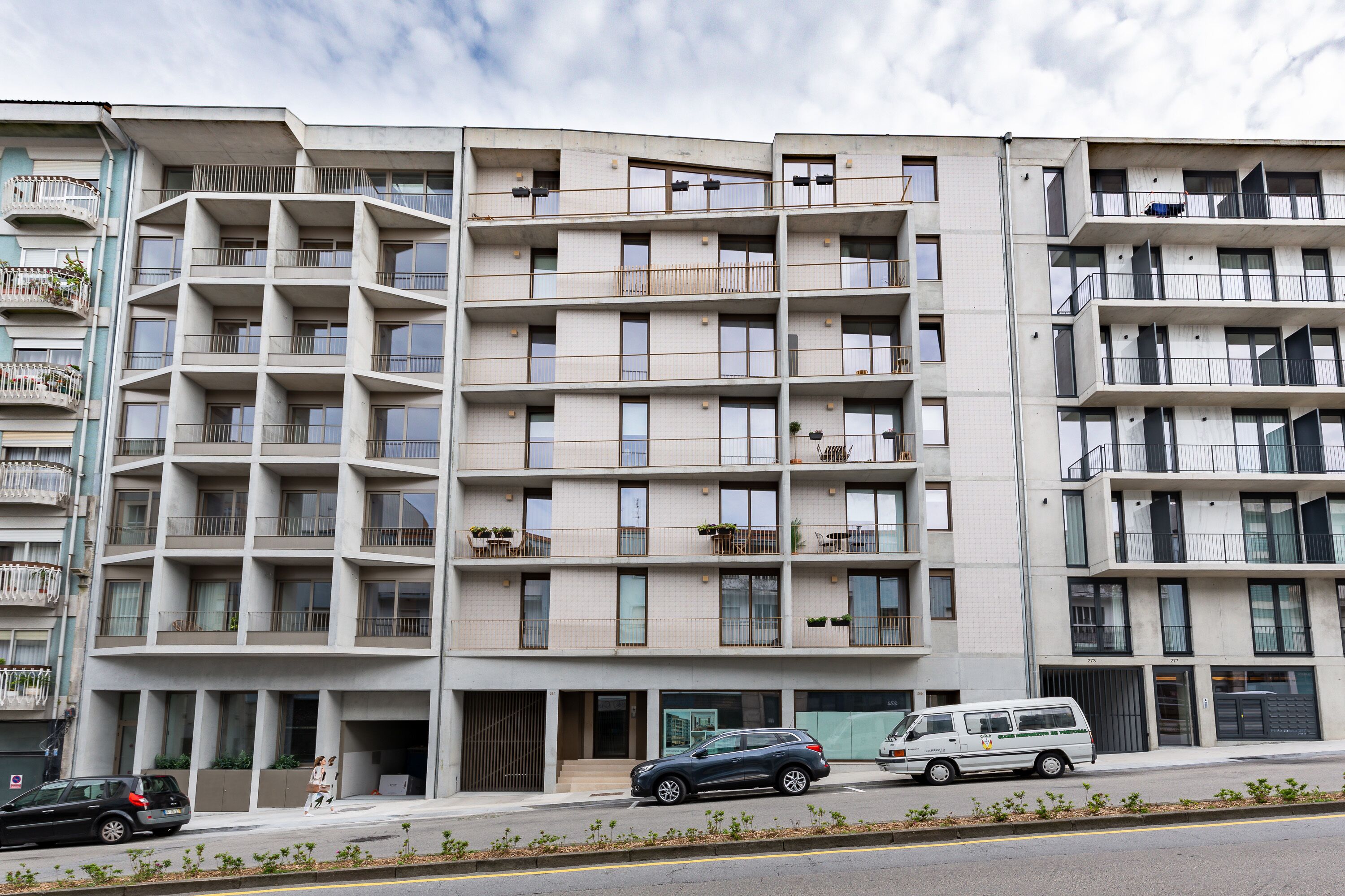 A multi-story residential building with balconies, a gated entrance, and a van parked in front.