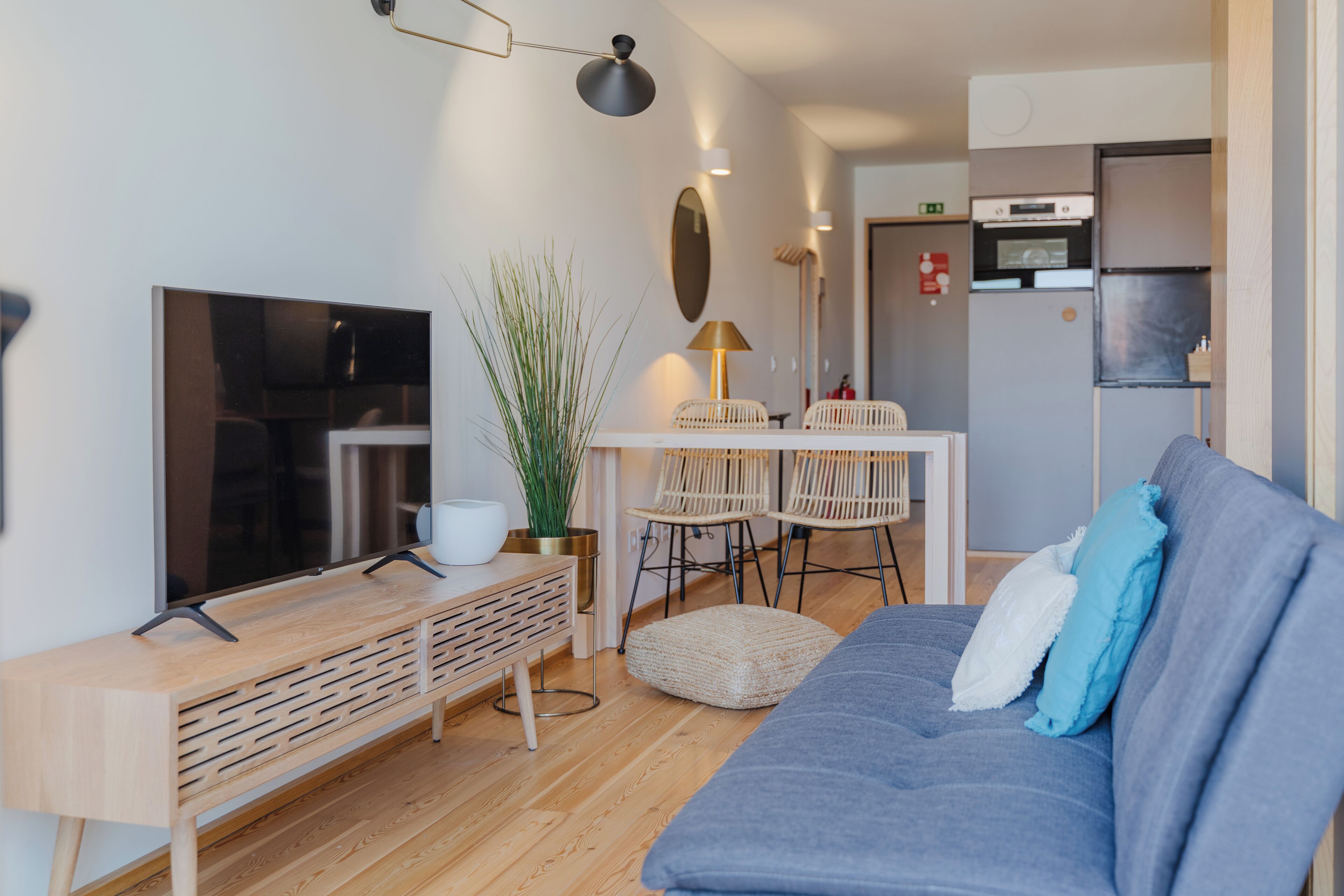 Una sala de estar moderna con un sofá, un televisor, un mueble bajo de madera y una zona de comedor con sillas y una mesa.