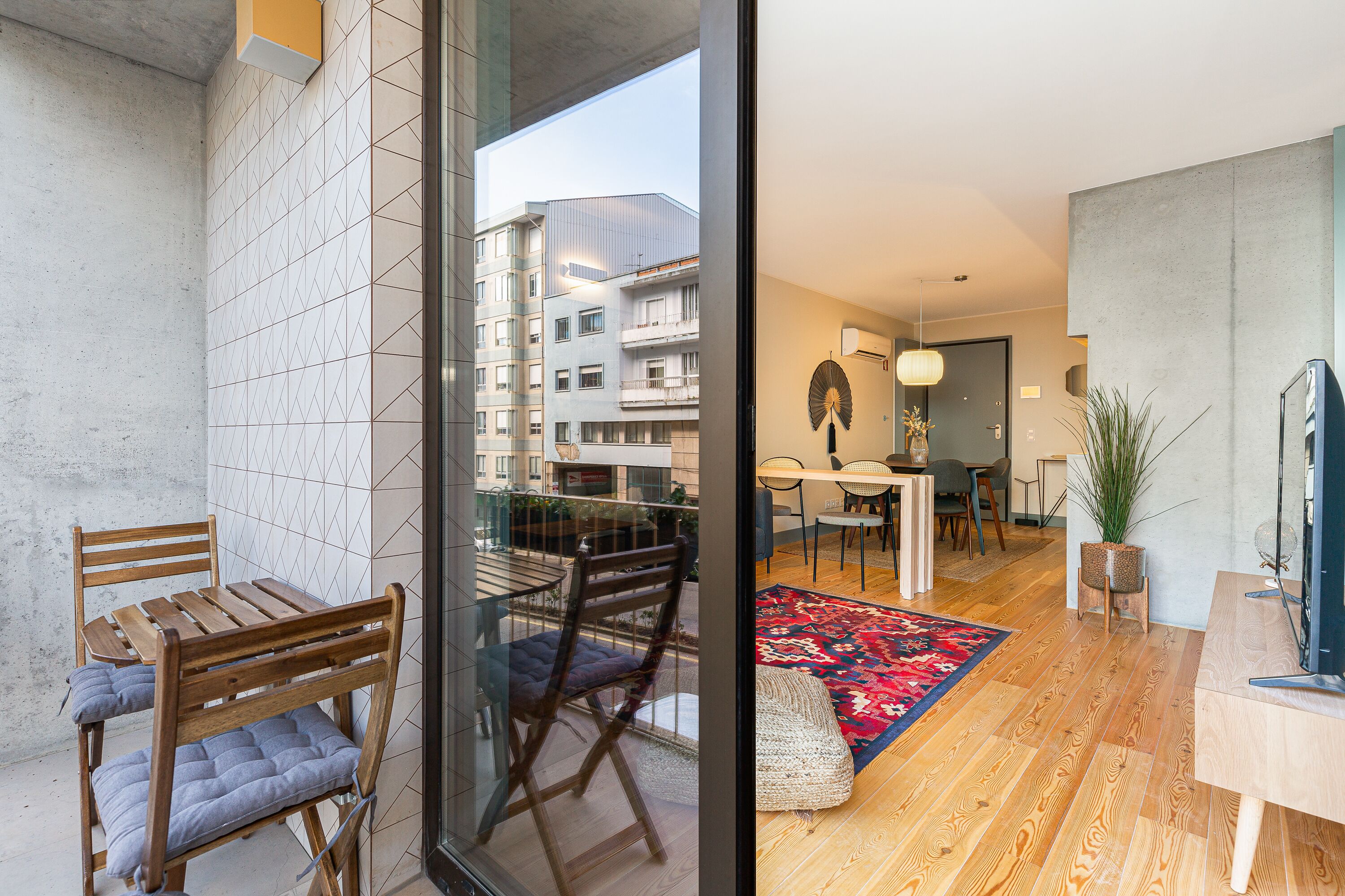 A modern apartment with a balcony, a dining area with a red rug, and a TV on a wooden table.