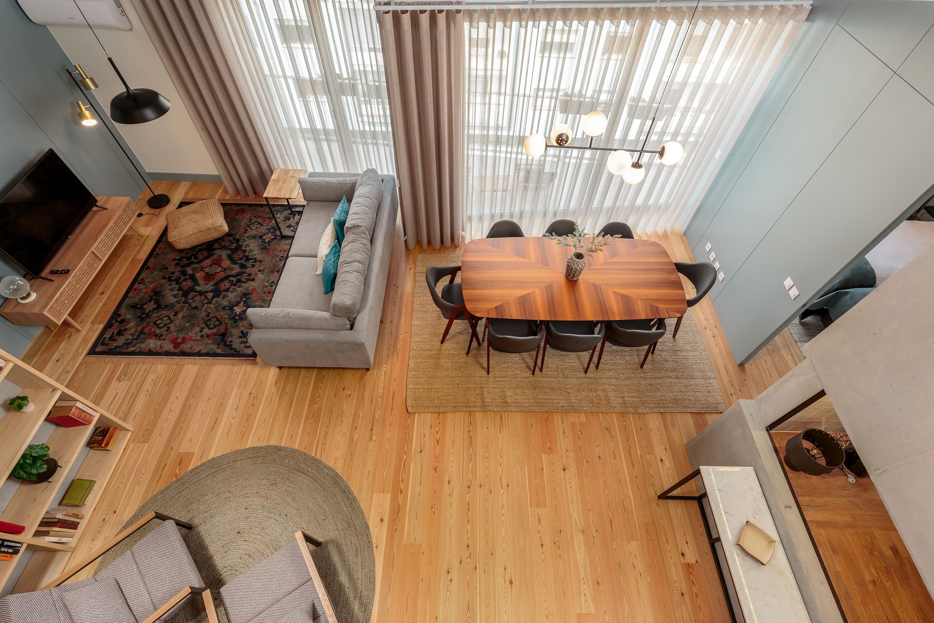 Un salon moderne avec un plancher en bois, un canapé gris, une table à manger avec des chaises, un téléviseur et une bibliothèque.