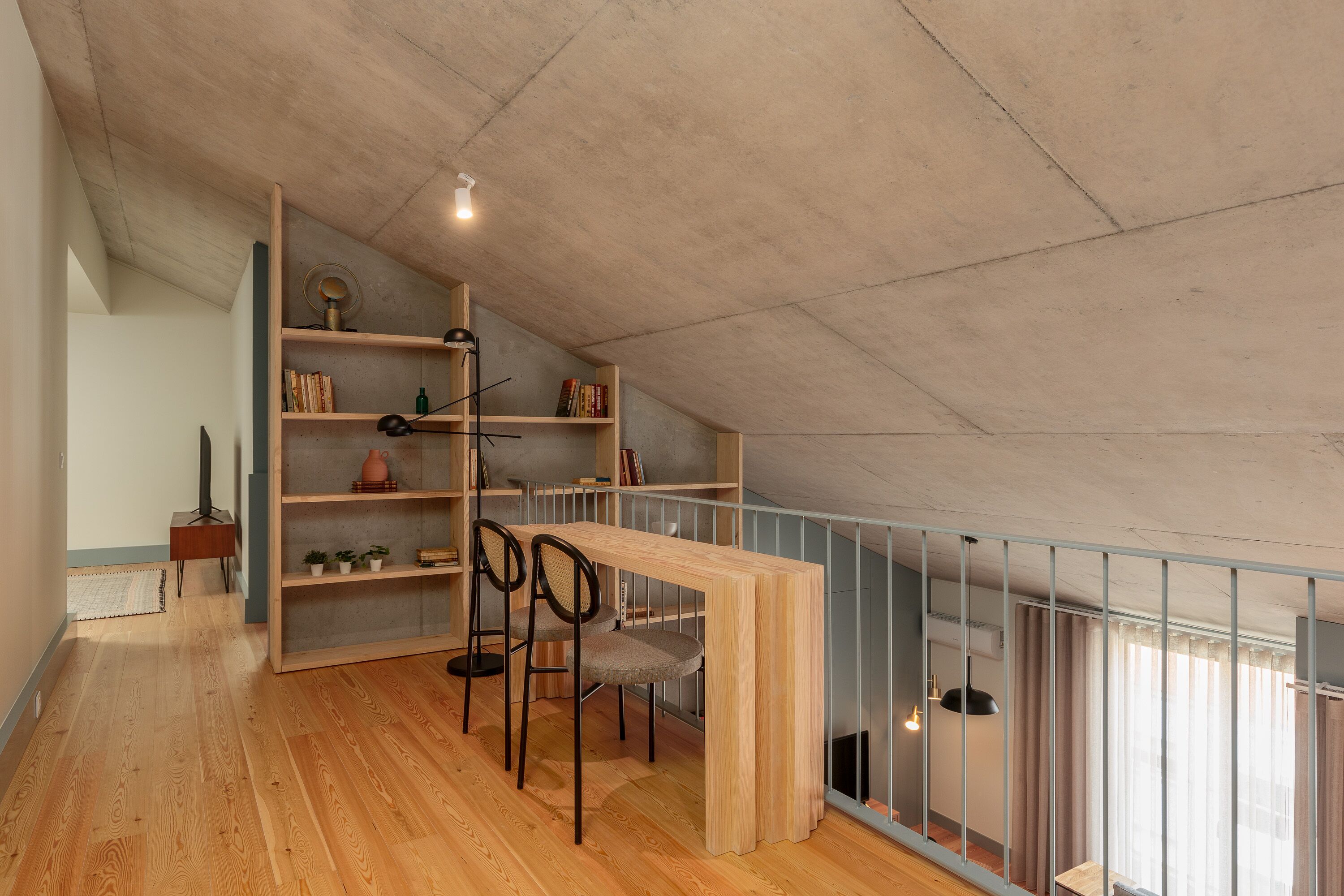 Ein Loft-Zimmer mit Holzboden, einer integrierten Bücherwand, einem Esstisch mit Stühlen und Blick durch eine Glasreling.
