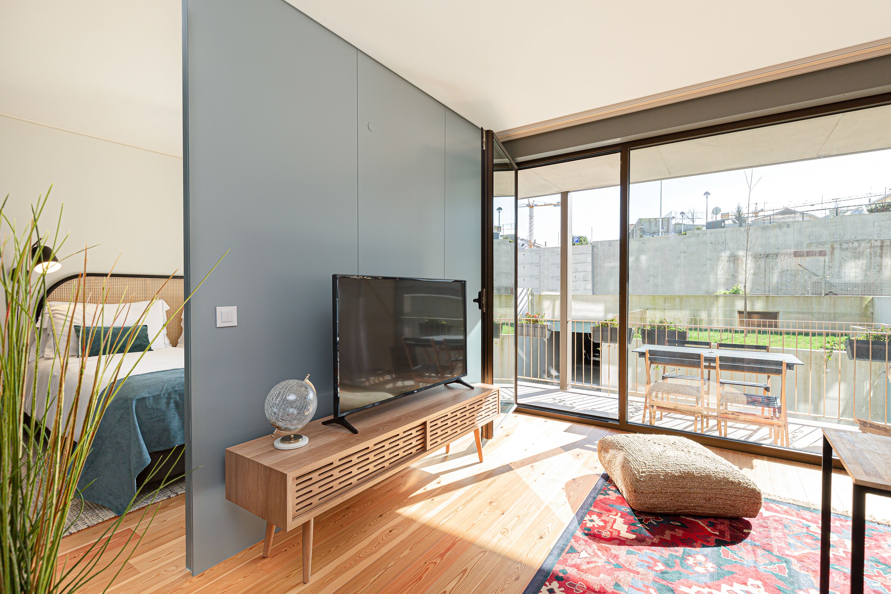A modern living room with a flat-screen TV on a wooden console, a large sliding glass door leading to an outdoor patio with a table and chairs.