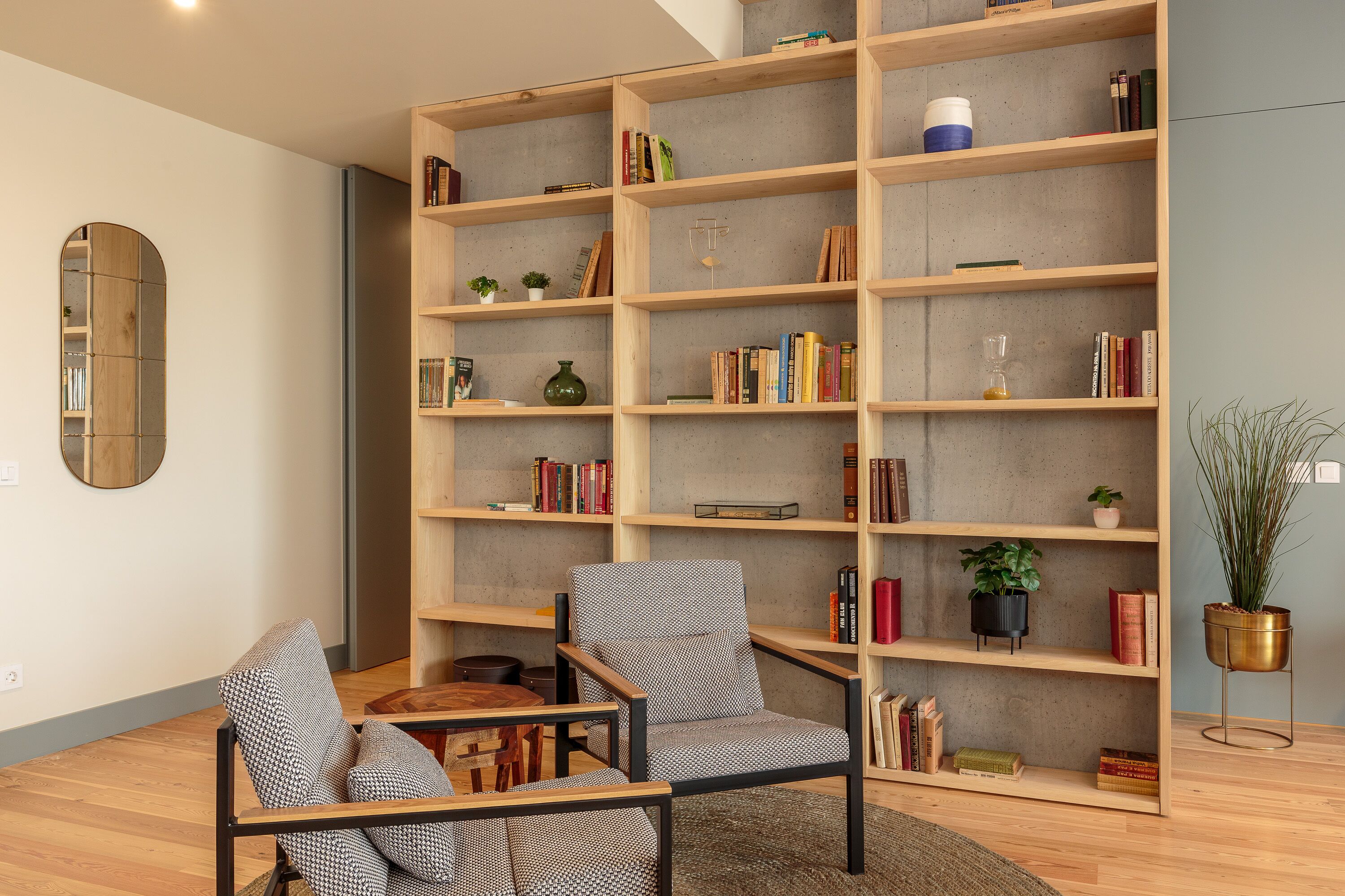 A modern living room with a large wooden bookshelf, two patterned armchairs, and a small table.