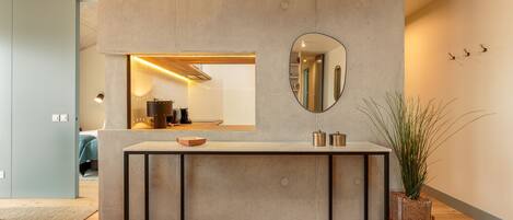 A modern kitchen with a concrete countertop, a round mirror, and a potted plant.