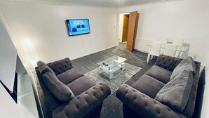 A living room with a gray sectional sofa, a glass coffee table, and a flat-screen TV mounted on the wall. - Modern 2 Bedroom Apartment With Free Parking (Glasgow)