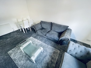 A modern living room with a grey sofa, a glass coffee table, and a tufted armchair. - Modern 2 Bedroom Apartment With Free Parking (Glasgow)