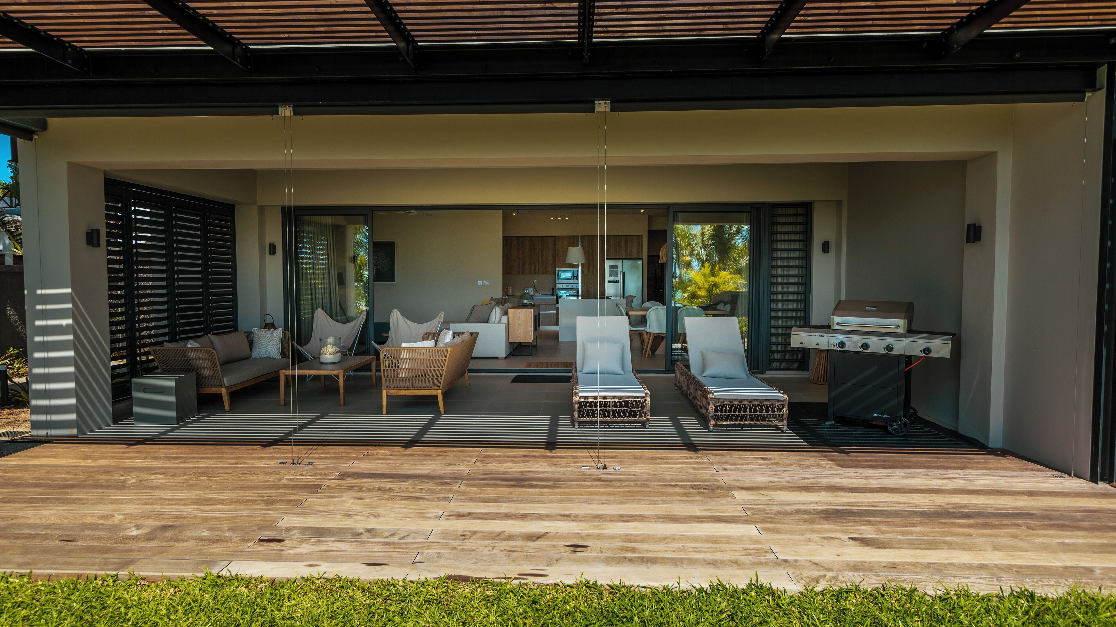 A modern outdoor living area with a wooden deck, lounge chairs, and a barbecue grill.