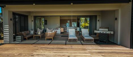 A modern outdoor living area with a wooden deck, lounge chairs, and a barbecue grill.