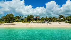 Une plage à l’eau turquoise et limpide, un rivage sablonneux et un complexe hôtelier comprenant plusieurs bâtiments et des palmiers.