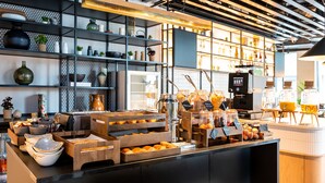 Een ontbijtbuffet met diverse etenswaren en drankjes, planken met keukengerei en een koffieapparaat.