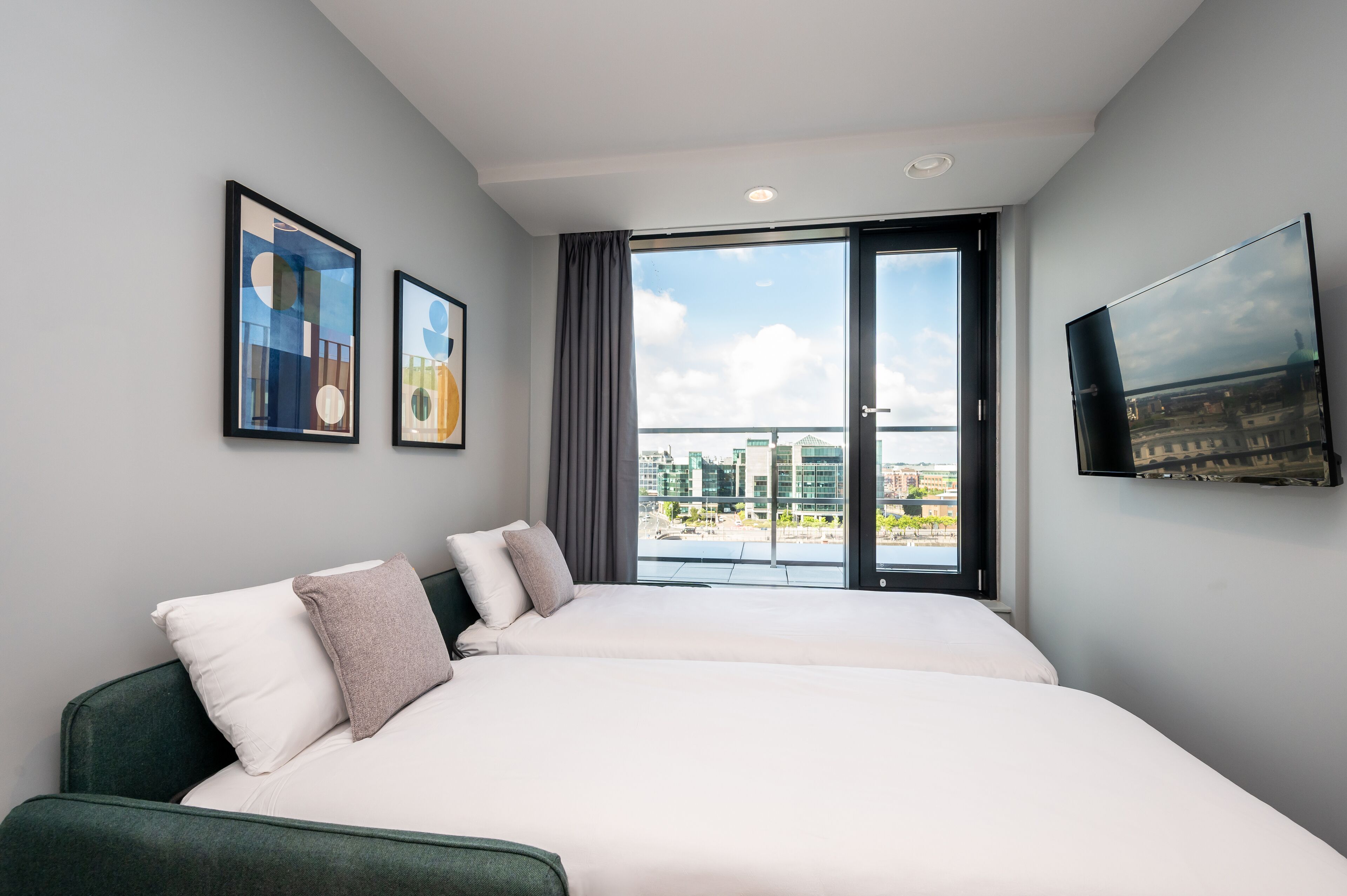 A modern hotel room with a large bed, a flat-screen TV, and a balcony with a city view.