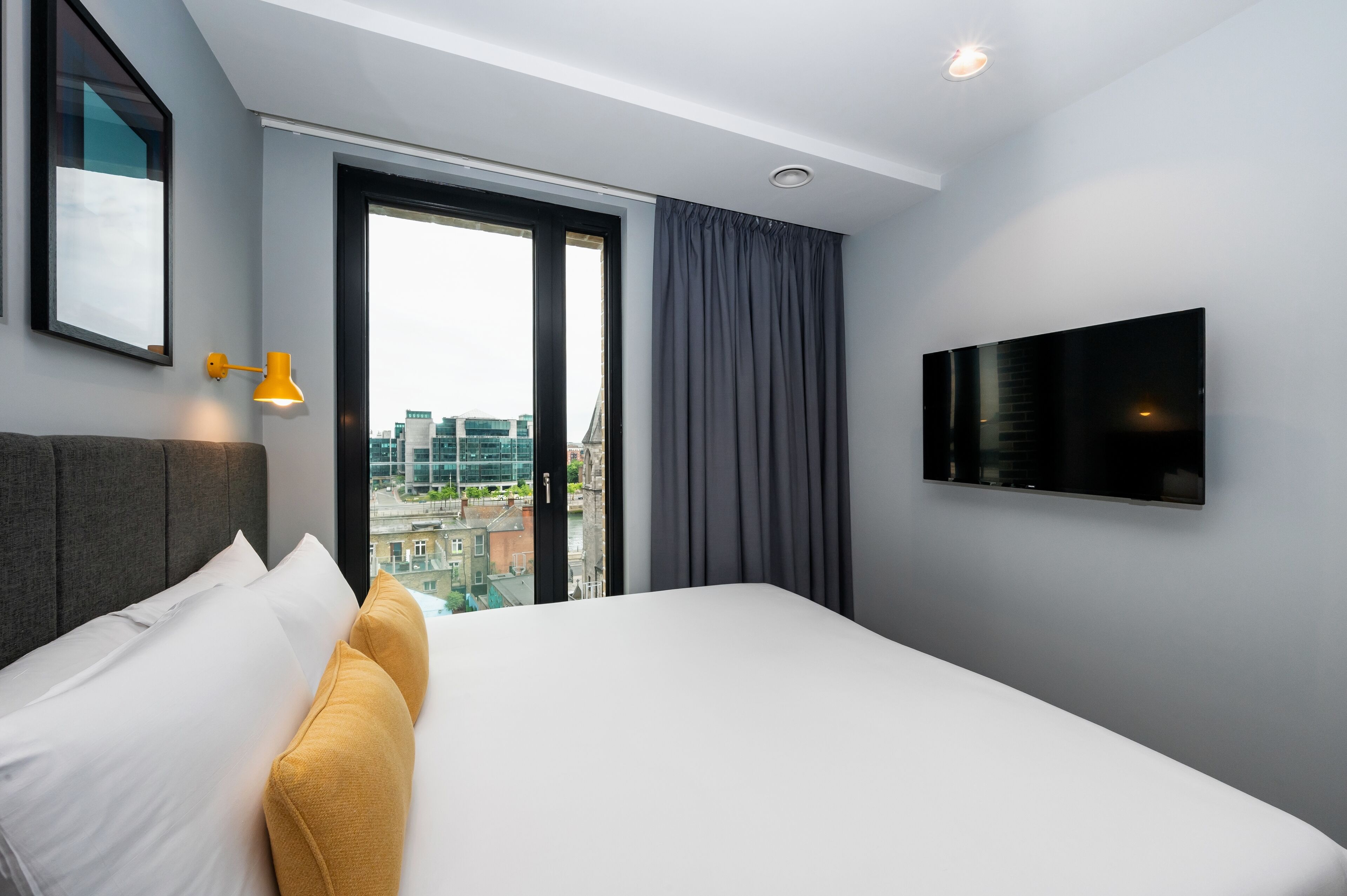 A hotel room with a large bed, a flat-screen TV, a city view, and a modern design.