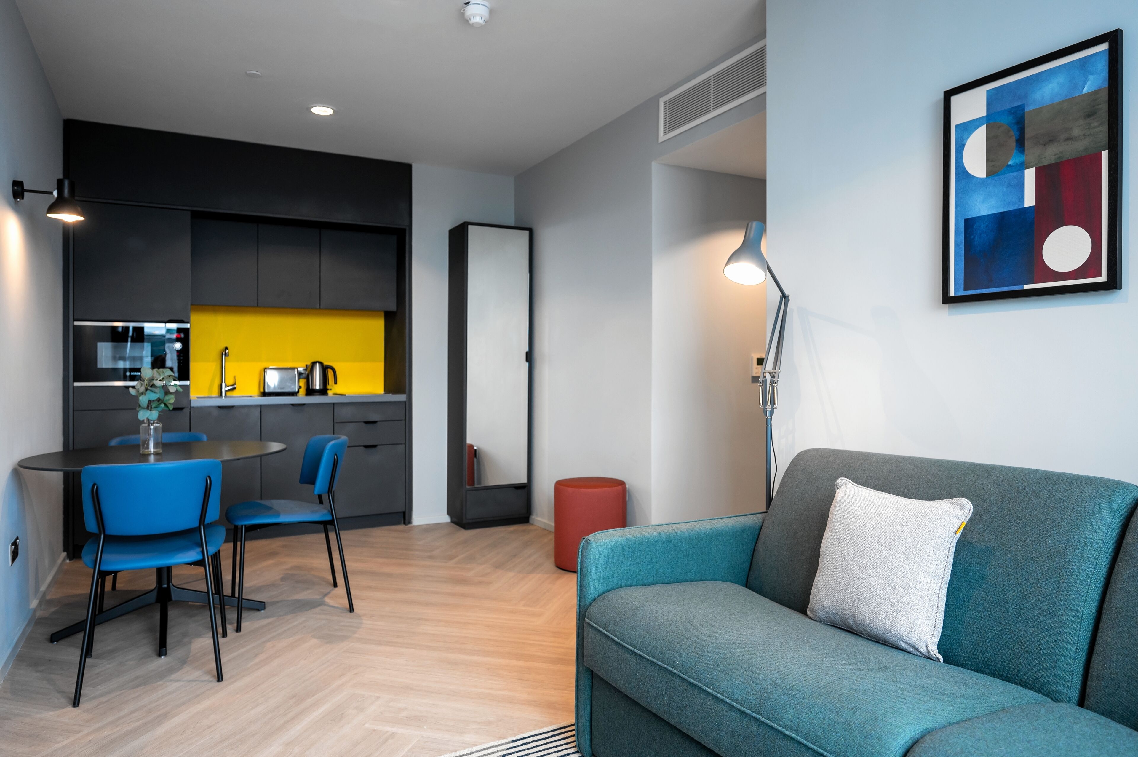 Un salon moderne avec un canapé de couleur turquoise et un coin repas doté de chaises bleues et d’un mur d’accent jaune.