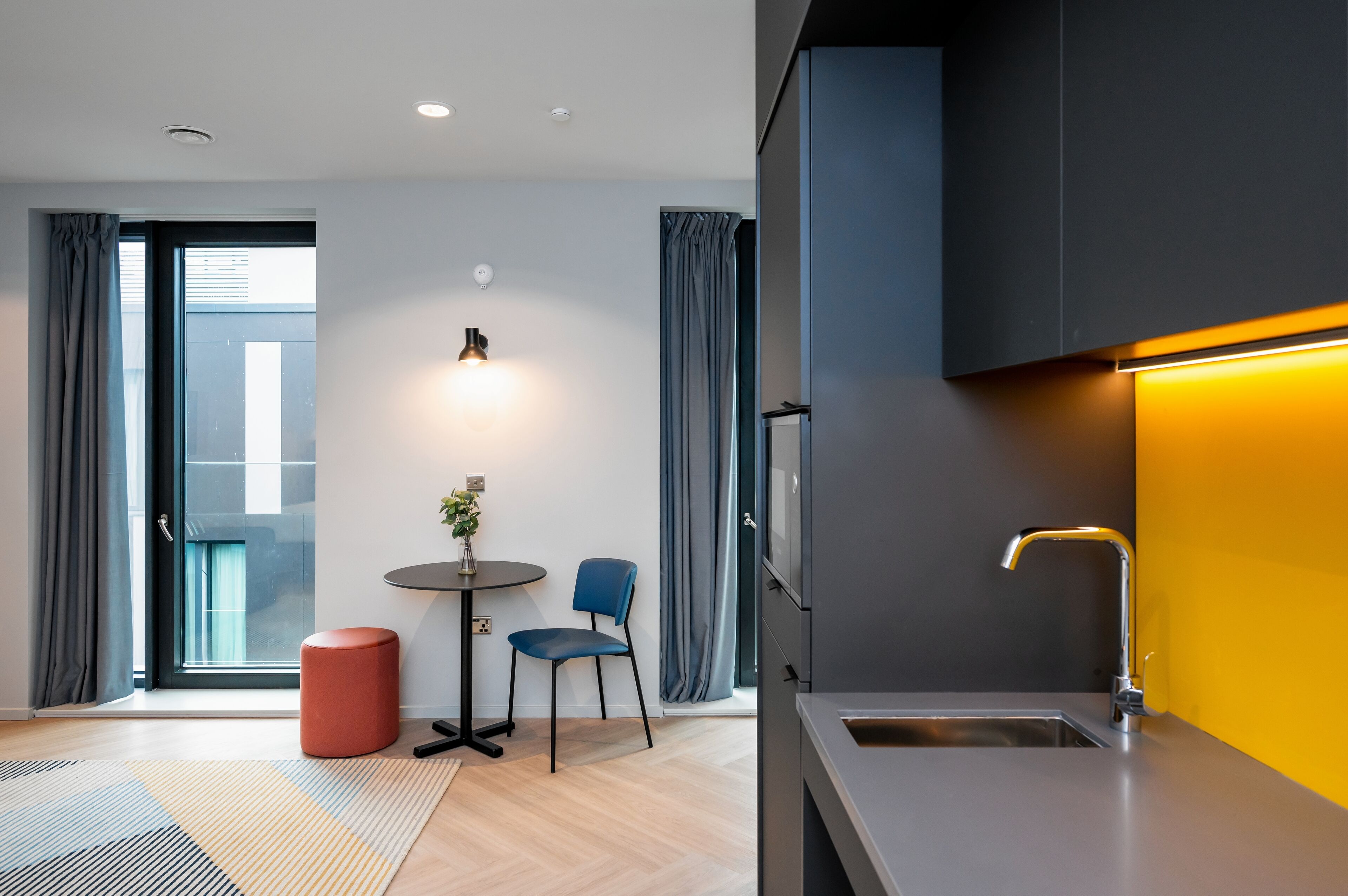 A modern kitchen with a grey countertop, a stainless steel sink, and a yellow accent wall.