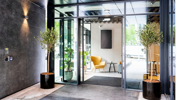 Een moderne entree met glazen deuren, plantenpotten, een gele stoel en een kleine tafel.