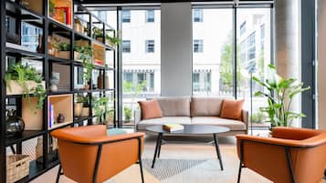 Una sala de estar moderna con un sofá, dos sillones, una mesita de centro y una estantería llena de libros y plantas.
