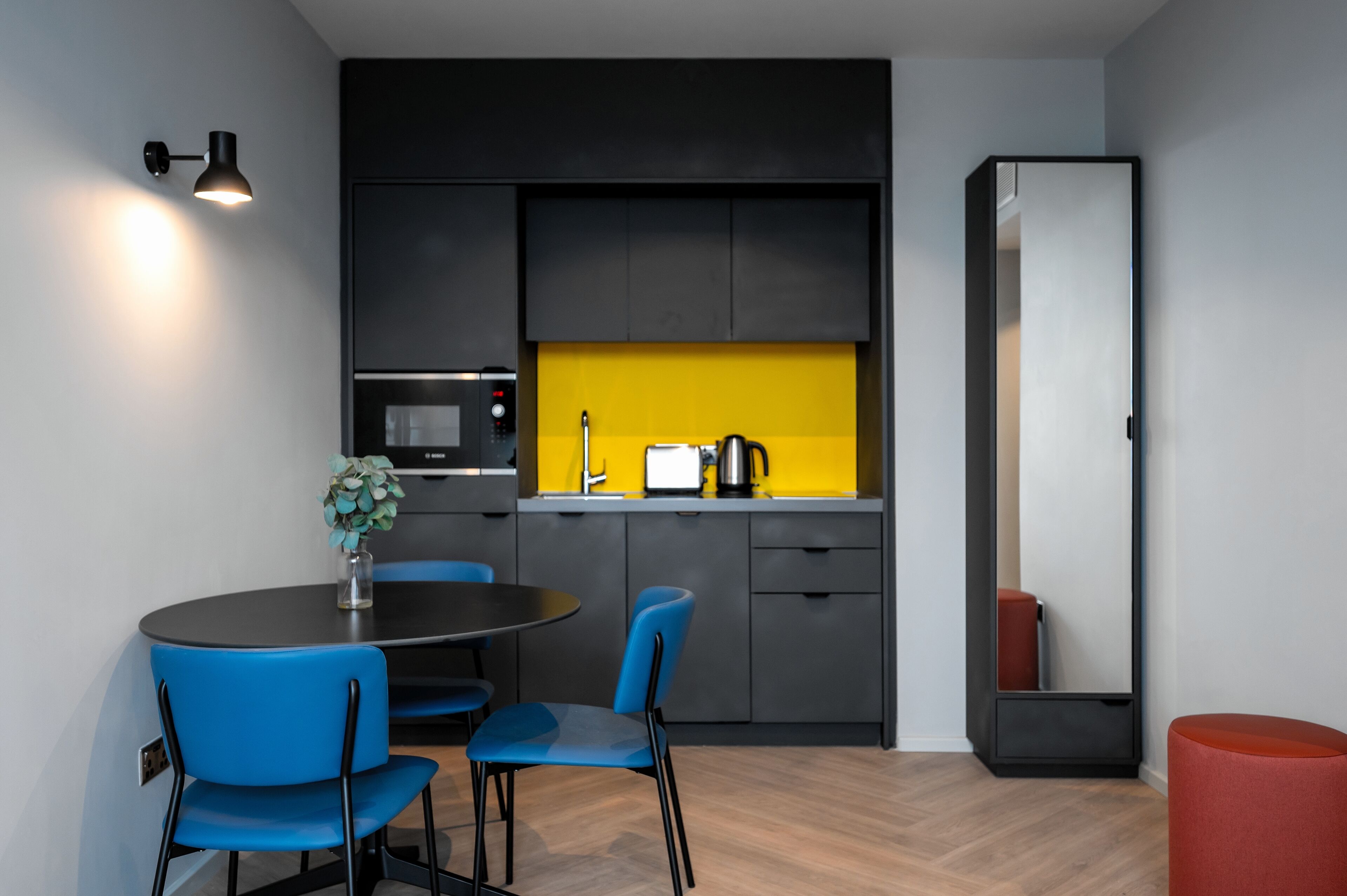 Une cuisine moderne avec des meubles noirs, un pare-feu jaune et un coin repas avec des chaises bleues.