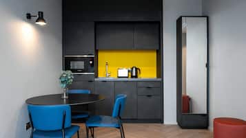 Une cuisine moderne avec des meubles noirs, un pare-feu jaune et un coin repas avec des chaises bleues.
