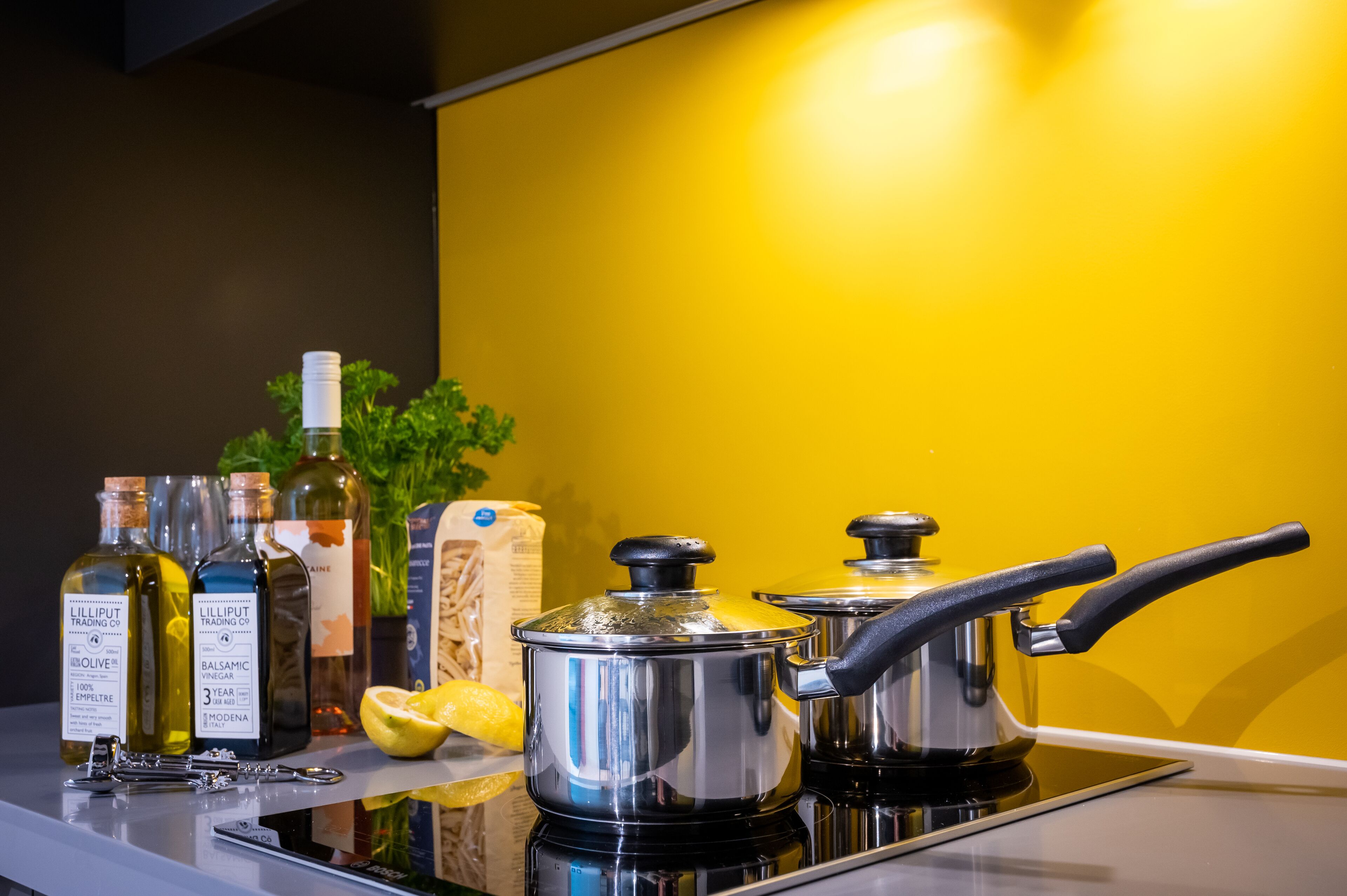 A kitchen counter with cooking pots, bottles of olive oil, balsamic vinegar, and a lemon.
