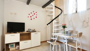 A modern living room with a TV, white furniture, a spiral staircase, and a small dining area. - Romantico Oltrarno - Sweet Dreams in Florence (Firenze)