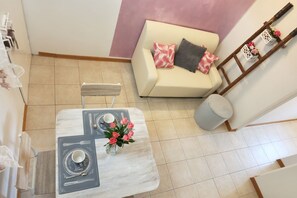 A dining area with a table set for two, a sofa with decorative pillows, and a ladder with lanterns against the wall.